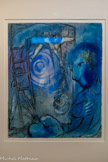 <center>La descente de Croix sur fond bleu</center>circa 1950. Gouache et encre sur papier. Achat, 2023.
« Pourquoi bleu ? Mais je suis bleu, comme Rembrandt était brun. » Ainsi s'exprimait Chagall sur cette couleur qui inonde l'espace pictural de La Descente de croix sur fond bleu d'une paix mystérieuse et qui ondule sur la toile, insufflant une sensation de rêverie.
Réalisée vers 1950, cette œuvre présente l'artiste vu de profil, une palette à la main, peignant une descente de croix. Cette œuvre fait partie des nombreux autoportraits de Chagall : au fil des années, ces portraits deviennent des représentations symboliques de la figure de l'artiste.
Ayant vécu son enfance dans une famille juive de Russie, Chagall acquiert une connaissance approfondie de la Bible, qui l'amène très tôt à réaliser des œuvres dont les sujets sont tirés de la Bible hébraïque (Ancien Testament). Il complète cette iconographie par des représentations du Nouveau Testament, à l'instar des crucifixions et des descentes de croix, qui prennent un sens différent au regard des tragédies du XXe siècle. Outre la dénonciation du martyr du peuple juif, Chagall souligne dans La Descente de croix sur fond bleu le transfert de la douleur du Christ à celle de l'artiste-créateur.