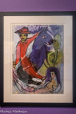<center>Le Cavalier mexicain en rouge et son cheval violet</center>1943.
Gouache, pastel, encre de Chine et grattage sur papier
Achat, 2023.
Acquise en vente aux enchères en avril 2023, Le Cavalier mexicain en rouge et son cheval violet complète la collection du musée sur la période américaine de Chagall (1941-1948), composée actuellement d'une seule huile sur toile, La Route de Cranberry Lake acquise en 2012, et d'une eau-forte, L'Ecuyère et le violoniste. Elle diversifie la collection, initialement centrée sur les œuvres bibliques, par des thèmes en lien avec les arts du spectacle.
Le Cavalier mexicain en rouge et son cheval violet est réalisé au moment où Chagall est en exil aux États- Unis, de 1941 à 1948. A cette période, Chagall réalise de nombreux projets pour les ballets, notamment les décors et costumes d’Aleko (1942) puis de L'Oiseau de feu (1945). Chagall arrive à Mexico un mois avant la première d’Aleko qui eut lieu le 8 septembre 1942. Il peut ainsi s'imprégner des couleurs chatoyantes du Mexique, restituées dans de nombreuses esquisses empreintes d'hispanisme.
L'année suivante, en 1943, il poursuit ses recherches dans un ensemble de gouaches singulières dites « mexicaines ». Cette série exprime sa profonde sympathie pour ce pays et ses habitants, mais aussi l'accord intime entre l'homme et la bête, thème chagallien par excellence.