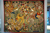 <center>Le musée Dom Robert et de la tapisserie du XXe siècle</center>Garden party
D’après DOM ROBERT (1907-1997)
Tapisserie de basse lisse. Laine et coton.
Atelier Tabard, Aubusson, 1956. Carton de tapisserie, 1956 224 x 278 cm. <br>Le titre de l’œuvre témoigne de la période anglaise. Le fond uni et le cadre rouge rappellent les tapisseries anciennes. Les fleurs ne sont pas encore celles des champs, mais celles cultivées en plate-bande dans le jardin monastère. Le bestiaire habituel de Dom Robert est présent dans u stylisation encore très marquée. Le lévrier afghan, rarement représenté mais figurant dans les carnets de dessins, est le sujet d’une au' tapisserie anglaise intitulée Pastoral (1955). Le chien joue les trouble-fête dans la basse-cour : c’est ici l’animal totem de l’artiste vigilant, « l'homme aux cent yeux » auquel rien n’échappe, soucieux de maintenir l’ordre autour de lui comme le fait l’artiste dans la composition de ses tapisseries.