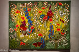 <center>Le musée Dom Robert et de la tapisserie du XXe siècle</center>Une de mai.
D’après DOM ROBERT (1907-1997)
Tapisserie de basse lisse, Exemplaire Hors Commerce. Laine et coton
Atelier La Beauze, Aubusson, 2002 Carton de 1974 168 x 213 cm<br>
Le titre évoque le nom d’une jument célèbre à l’époque dans les champs de courses. Une de mai est une évocation printanière, sans chevaux ni poneys. Quatre ans plus tard, son double Vasca, nom du petit chien berger des Pyrénées représenté à la place du chat, montre l’habileté de Dom Robert à créer une variation sur un même thème. Le jeu des regards est la clé de la scène. Dans Une de mai, le chat, indifférent, passe inaperçu - ce qui est bien dans sa nature - près des deux coqs qui se font face. Tandis que le chien Vasca, pataud et massif, qui le remplace dans l’autre version, s’est fait repérer par le coq de gauche, un des éléments redessinés ici par Dom Robert.