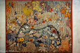 <center>Le musée Dom Robert et de la tapisserie du XXe siècle</center>La Vie douce
D’après DOM ROBERT (1907-1997).
Tapisserie de basse lisse. Exemplaire 1. Laine et coton. Atelier Tabard, 1952. Carton de 1952, 240,5 x 299,5 cm <br>
En Angleterre, Dom Robert s’attache encore à la nature domestiquée des jardins. Ici, une mare constitue le centre de la composition. Des poissons étranges, déjà présents dans l’enluminure La Pêche miraculeuse de 1934, y nagent parmi les nénuphars blancs. Ce monde aquatique est environné d’une végétation luxuriante d’ajoncs et de fougères dans lesquels se cachent paons, perruches, coqs et canards. Leurs plumages précieux se confondent avec les feuillages aux verts déclinés sur tous les tons, à l’image des verdures médiévales. Cet exemplaire a subi l’épreuve du temps. Les verts ont perdu de leur intensité et ont viré au bleu... Mais l’harmonie de la composition est préservée.