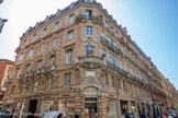 <center>Toulouse</center>Rue d'Alsace-Lorraine. Ancien Grand hôtel Tivollier. Un hôtel de voyageurs est construit entre 1872 et 1873 sur les plans d'Isidore Villamur pour le compte d'Auguste Tivollier. Au carrefour de la rue Baour-Lormian, l'angle coupé concentre l'essentiel de l'ornementation. Le rez-de-chaussée et l'entresol sont réunis par une arcade de boutique en plein cintre. Elle a conservé son chambranle mouluré et une agrafe qui porte un cadre, soutenu de branches de laurier et encadré de deux nymphes tenant un sceptre à pignon et une grappe de raisin. Au 1er étage, la fenêtre a un chambranle mouluré, un garde-corps à balustres en pierre et une agrafe sculptée.