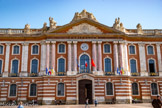 <center>Le Capitole.</center>Au centre, l'avant-corps, large de trois travées, est ouvert par une grande porte cochère dont l'agrafe porte les armoiries sculptées de la ville, surmontées d'une corniche curviligne. Aux étages, les huit colonnes symbolisent les huit capitoulats de la ville. D'ordre colossal, embrassant les deux étages, en marbre rose, elles ont des chapiteaux ioniques qui soutiennent un entablement gravé de l'inscription « CAPITOLIUM », surmonté d'un fronton rectangulaire où prennent place les armoiries de la République française[