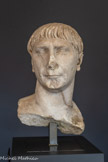 <center>Musée Saint-Raymond</center>Buste fragmentaire de Trajan.
Empereur de 98 a 117 Marbre de Goktepe (Turquie).
Type dit « des Decennalia ». Vers 10
<br> Après Nerva, le pouvoir est concentré entre les mains de six empereurs : Trajan, Hadrien, Antonin le Pieux. Marc Aurèle (associé un temps à Lucius Verus) et Commode. Ces empereurs, aux règnes particulièrement longs, forment la dynastie des Antonins, du nom d'Antonin le Pieux qui, mieux que tout autre, symbolise la stabilité de l'Empire. Trajan est issu d'une famille de colons italiens installés dans la province de Bétique (actuelle Andalousie) à Italica (actuelle Santiponce. près de Séville). Il accède au pouvoir après avoir été adopté par Nerva et épouse Plotine, originaire de Nîmes. Il conquiert la Dacie (actuelle Roumanie) et entreprend de grandes campagnes en Orient. On lui doit aussi la construction de monuments parmi les plus célèbres de la Rome antique.