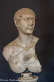 <center>Musée Saint-Raymond</center>Buste de Trajan (53-117). Empereur de 98 à 117 Marbre blanc de Carrare Type dit « du sacrifice » Entre 108 et 113.  <br>L'évolution des portraits de Trajan est dictée par les grands événements de son règne. Son effigie est connue par quatre types qui se différencient bien souvent par la seule disposition des mèches de cheveux. La chevelure, coupée « au bol » et peignée de l'arrière vers l'avant sur les portraits les plus anciens de Trajan, est ici plus compliquée et annonce celle des effigies de l'époque d'Hadrien, son successeur. La disposition des mèches suit un schéma très spécifique qui apparaît sur des scènes de sacrifice de la Colonne de Trajan, d'où le nom donné à ce type iconographique nouveau. Le torse nu était peut-être, à l'origine, en partie revêtu de l'égide (la cuirasse de la déesse Athéna/Minerve, donnée par Zeus/Jupiter), comme le montrent deux autres bustes, conservés à Copenhague et à Munich.