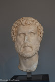 <center>Musée Saint-Raymond</center>Antonin le Pieux (86-161)
Empereur de 138 à 161 Marbre de Goktepe (Turquie). <br>
Pour exécuter un portrait officiel en plusieurs exemplaires, le sculpteur reproduisait fidèlement un prototype officiel, en plâtre ou en terre, qui servait de référence pour toutes les copies exécutées dans un matériau noble. Un compas et un fil à plomb permettaient de reporter sur le bloc de marbre les points de repère, sélectionnés sur le modèle à copier.
Ce portrait de grande qualité, conçu à Rome, montre encore trois petites « verrues », derrière la tête, oubliées par le sculpteur chargé du polissage final. Ces points de mesure prouvent que sur les meilleurs exemplaires sortis des ateliers de la capitale, l'arrière était copié avec autant de soin que le visage. Ce portrait fut probablement envoyé à Chiragan peu après l’avènement d'Antonin le Pieux afin de compléter la série des effigies impériales de ce domaine.