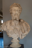 <center>Musée Saint-Raymond</center>Portrait de Septime Sévère (145 – 211). Empereur de 193 à 211 Marbre de Goktepe (Turquie)
Type II dit « de l'adoption »
Entre 195 et 200. <br>
Comme pour Trajan, pas moins de quatre portraits de Septime Sévère ont été découverts à Chiragan. C'est tout à fait exceptionnel. L'atelier romain à l'origine de ce buste est peut-être aussi l'auteur de deux autres, de même type, conservés à Copenhague (Ny Carlsberg Glyptotek) et à Rome (Palazzo Massimo aile Terme). Une armure à écailles (lorica squamatfa) porte en son centre la traditionnelle tête de Gorgone, censée pétrifier l'ennemi.
En 195, Septime Sévère se proclame fils de Marc Aurèle et donc frère de Commode. Comme sur les monnaies, le profil du portrait en marbre de Septime trahit le désir de se rapprocher formellement de ces empereurs antonins, dirigeants exemplaires, notamment du type cuirassé de Marc Aurèle, exposé ici-même.
