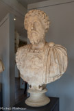 <center>Musée Saint-Raymond</center>Buste cuirassé de Marc Aurèle âgé 121 - 180
Empereur de 161 à 180 Marbre d’Afyon (Turquie)
Type IV (variante A)
170 - 180. <br>
Les portraits des dernières années du règne de Marc Aurèle sont caractérisés par une grosse mèche axiale en flamme autour de laquelle s'organise toute la coiffure, une barbe en pointe et une moustache dont les extrémités s'enroulent vers le haut. C'est probablement la mort subite de Lucius Verus, en 169, mais aussi la célébration des dix ans de règne, en 171, qui ont motivé la création de ce nouveau type de portrait représentant l’empereur philosophe dans les dernières années de son règne. Fait exceptionnel, il fut probablement créé en dehors de Rome, en Pannonie (actuelle Autriche), où Marc Aurèle dut se rendre pour rétablir l'ordre dès 169. Très proche d’un exemplaire conservé à Rome, cette œuvre se distingue cependant par un protège-nuque presque collé au cou qui donne, de profil, l’impression d’une cuirasse trop petite. Tête et buste auraient-ils été conçus par deux sculpteurs différents ?
