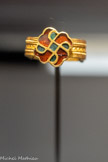 <center>Musée Saint-Raymond</center>Bague en or, grenat ou verroterie, pâte de verre. Deuxième moitié du Ve siècle - début du VIe siècle. Fouille Bureau d'investigations archéologiques Hadès (2018). Boulbènes des Vitarelles (Seysses). Tombe dite de la « Dame de Seysses ». <br>
Cette bague exceptionnelle présente un décor cloisonné de grenats sur paillon (fond d'or) et de pâte de verre. Le motif décrit un svastika dont les quatre branches forment des têtes d'aigle. Observez la surface extérieure de l'anneau : elle est composée de plusieurs fils parallèles soudés. Cette bague est unique mais elle peut être rapprochée des parures caractéristiques de la culture germanique orientale (dont les Wisigoths) où l'on trouve de nombreux motifs à têtes de rapace.