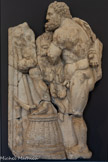 <center>Musée Saint-Raymond</center>Hercule et le roi Augias. Cinquième des douze travaux. Grèce, Péloponnèse.
Le roi Augias, fils du Soleil (Hélios), possédait d'immenses troupeaux. Mais il négligeait de faire nettoyer ses écuries. L'accumulation du fumier rendait les terres environnantes stériles. Eurysthée voulut humilier Hercule (l'Héraclès grec) en lui confiant cette tâche habituellement réservée aux esclaves. Pour assainir ces écuries, le héros détourna le cours de deux fleuves, l'Alphée et le Pénée, pour qu'ils nettoient tout sur leur passage.
Sur ce relief, le héros, le pied posé sur un panier renversé dont il ne s'est pas servi, regarde les eaux des fleuves nettoyer les écuries. Encore une fois, son attitude rappelle des images de dieux grecs qui ont souvent servi d'exemple dans l'art romain. Comme sur la statue d'Hercule exposée précédemment, la main ramenée dans son dos souligne le repos après l’action. Contrairement aux premiers travaux, la physionomie du héros a changé : sa barbe a poussé, il a vieilli. Au fur et à mesure de ses succès, il acquiert la sagesse et se rapproche donc de sa divinisation et sa représentation devient celle des dieux gréco- romains : Jupiter, Pluton, Esculape.