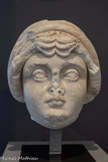 <center>Musée Saint-Raymond</center>Portrait de Galeria Valeria Eutropia (?)
Epouse de Maximien Hercule, mère de Maxence et de Fausta Années cinquante du IIIe siècle - 330 Marbre de Saint-Béat (Haute-Garonne)
Fin IIIe - premières années du IVe siècle. <br>
La coiffure rappelle celle d'Hélène, épouse de l’empereur Constantin. Cette mode est apparue à la fin du IIIe siècle. Sur certains sarcophages de la première moitié du IVe siècle, des femmes de très haut rang sont également coiffées de la sorte. Un rouleau de cheveux encadre le visage, une grande tresse forme un « turban » qui, depuis l'arrière, remonte en bandeaux aplatis se glissant sous les enroulements du dessus et s'achevant au milieu du front en huit mèches frisées au fer. Ce portrait peut être relié aux trois autres têtes présentées ici. Il s'agit donc d'un très rare groupe dynastique.