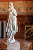 <center>Le château Laurens</center>Non signée, la statue en marbre blanc figure un personnage féminin debout et entièrement voilé, croisant ses mains sur sa poitrine, et s'inspirant fortement de la sculpture médiévale allemande dite belle madone de Nuremberg dont plusieurs copies ou modèles ont été diffusés au 19e siècle (en particulier un buste aujourd'hui conservé au Louvre). Documentée par une photographie ancienne en noir et blanc, la sculpture a probablement été commandée par Emmanuel Laurens pour orner son bureau en complément des autres meubles, et avait été remisée depuis plusieurs décennies dans une caisse en bois, avant d'être réinstallée en 2022 avec son piédestal d'origine en pierre. A droite, le tabouret à deux pieds appuyé contre la partie à grand vantail de l'armoire.