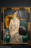 <center>Femme aux bijoux.</center>KEES VAN DONGEN, (1877-1968). Huile sur toile, 1929.
II s'agit avec Femme aux bijoux d'un magnifique exemple de l'art de Van Dongen dans les années 1920. Une jeune femme non identifiée dont l'apparence saisissante, la robe précieuse et les bijoux, loi donne éclat et audace, arbore les caractéristiques typiques des portraits les plus glamours de l'artiste.
Vêtue d'une robe de soirée élégante, sa beauté est accentuée par la brillance de sa chevelure et par les étincelants colliers et bracelets qu'elle porte et qui sont peints à l'aide d'empâtements. Les attributs, dont la fourrure posée sur le bord du canapé, laissent à penser qu'il s'agit d'une femme de la haute société, même si le peintre s'attarde plus à la féminité du modèle qu'à son identité. Le traitement subtil de sa chair et le reflet argenté de sa robe sont sublimés par le contraste avec le vert profond du canapé et de l'alcôve sombre de l'arrière-plan. Les reflets verts sur la peau du modèle montrent à quel point te peintre se soucie peu d'anatomie ou de représentation naturaliste mais privilégie la présence physique et sensuelle du modèle. Ils sont par ailleurs les derniers témoins éblouissants de la période fauve du peintre dont le point d'orgue se situe entre 1901 et 1914.