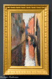 <center>Canal à Venise</center>HENRI MARTIN (1860-1943). Huile sur toile, ca.1910
Les zones de contacts entre terre et eau furent des lieux élus par Henri Martin pour leurs possibilités picturales. Une touche dissociée très libre pouvait en effet s'y exercer avec bonheur. Après Marseille et avant Collioure où il achète une maison en 1923, Venise fut un de ses séjours de prédilection dès les années 1900. Aux palais somptueux, aux monuments insignes et aux vastes perspectives du grand canal et de la lagune, il préféra souvent les vues plus intimes des petits canaux.
Ici le format vertical et la perspective accentuent l'impression d'étroitesse d'un rio enserré entre de hauts murs. L'apparente facilité de la composition, restituant l'illusion d'une réalité vécue par le spectateur, cache en fait un formidable savoir-faire. Un point de fuite central organise en effet le tableau autour des grandes lignes de fuite obliques de l'architecture des palais ; elles mènent l'œil vers la silhouette gris bleu d'un campanile à l'arrière-plan. Les verticales majeures des arrêtes de briques et de leurs reflets, les pans géométriques des murs rose orangé et ocre jaune, en lumière et très vifs à droite, dans l'ombre, assourdis de bruns et de gris, à gauche, s'agencent en un puzzle de couleurs.