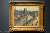 <center>La Seine, quai des grands Augustins.</center>ALBERT MARQUET (1875-1947). Huile sur toile.
 
Proche d’Henri Matisse, son ancien camarade de l’atelier Gustave Moreau, Marquet qui était présent à ses côtés dans la fameuse « Cage aux fauves » du salon d’automne de 1905, fut dès lors assimilé au fauvisme. C’est pourtant dans l’art des gris, et non dans les outrances de la couleur, que Marquet trouva son mode d’expression. Son art est celui de la synthèse : Marquet d’un trait de pinceau noir, donne l’essence du mouvement et de l’atmosphère.
Tout comme Matisse fut un grand maître de la surface par le décoratif, Marquet excella dans la peinture de l’étendue, celle du plan d’eau, du port d’Alger où il vécut longtemps, de Marseille, d’Arcachon ou de la Seine, à la Frette ou à Paris. D’abord installé à Paris quai Saint-Michel, puis en 1931 dans l’atelier du 1 rue Dauphine, à l’angle du quai des Grands-Augustins, il peint la Seine et ses quais. La vue du cinquième étage de la rue Dauphine lui permet de déployer l’espace de part et d’autre du bras du fleuve qui longe l’île de la Cité en faisant un coude. À droite, sur le quai bordé d’arbre, quelques passants et de rares automobiles animent cette belle matinée de fin d’automne. En face, Quai des Orfèvres, se détachent la silhouette de l’hôtel de Police et au loin, fantomatiques, celles du Pont-Saint-Michel et de Notre-Dame. La lumière froide est déjà pas pâle, les arbres dépouillés de leurs feuilles, tout évoque dans cette vue l’hiver qui s’approche.