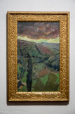 <center>La Pluie.</center>PAUL SERUSIER (1863 – 1977). Huile sur toile.
Artiste ultra doué, Paul Sérusier se trouve un octobre 1888 à Pont-Aven où sous la houlette de Gauguin, il peint Paysage au bois d’Amour. Ce dernier l’encourage à peindre en plein air des couleurs franches. De retour à Paris, il montre son œuvre, également appelé Le Talisman, à ses amis Maurice Denis, Bonnard, Ibels et Ranson qui se réunissent autour. Ensemble, ils fondent le groupe des Nabis, sans contour défini ni unité stylistique, Sérusier, le « Nabi à la barbe rutilante », retourne régulièrement Bretagne. Durant l’été 1899 avec Filiger, Gauguin et de Haan, il est pensionnaire de Marie Henry au Pouldu. Après un séjour à Pont-Aven où il rencontre Verkade et Ballin en 1891, il s’installe au Huelgoat, jusqu’à 1893.
La Pluie rappelle La Barrière, les thèmes, très simples, sont comme un retour aux sources. Ici, le paysage vallonné montre des parcelles de culture, toutes vertes, plus ou moins claires, délimitées par des haies très sombres. Le cyprès du premier plan renforce la verticalité de la composition. Derrière les nuages très sombres percent le soleil. La pluie n’est visible que par les petites touches fragmentées et au obliques dont use Sérusier.