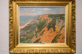 <center>Les falaises de Quimper.</center>MAXIME MAUFRA (1861 – 1918). Huile sur toile, 1905.
Élève du paysagiste Charles Leroux, Maxime Maufra s’initie à la peinture en plein air avec les frères Charles (1831 - 1911) et Alfred Leduc. En 1899, il abandonne le métier auquel le destine son père et se consacre exclusivement à la peinture. Maufra expose à la deuxième exposition des peintres impressionnistes et symbolistes en 1892 avec les peintres les plus avant-gardistes de son temps. En quittant la Bretagne, Maufra s’installe au Bateau-Lavoir à Montmartre.
Maufra montre ici qu’il est un virtuose du paysage. Ce peintre de la nature équilibre son tableau avec des couleurs chaudes d’été. La place majeure de la toile est occupée par la falaise rouge que quelques végétaux parsèment çà et là. En contrebas, proche de l’eau, une étendue verte légèrement cernée de noir rappelle que le peintre a parfaitement assimilé les enseignements de l’école de Pont-Aven. Le plan d’eau se distingue tandis qu’à l’horizon on aperçoit le rivage. Comme dans la plupart de ses œuvres, et fidèle à la leçon synthétiste, Maufra place très haut le ciel et lui accorde une place minime : une petite bande bleue traversée par quelques nuages gris. Ce ne sont pas des effets atmosphériques qui l’interpellent, mais la nature dans toute sa force