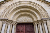 <center></center><center>Beaumes-de-Venise. </center> Eglise saint Nazaire. Le tympan au-dessus du portail d'entrée s'inspire d'un décor antique de la chapelle Saint-Quenin de Vaison-la-Romaine. Il représente un vase d'où sortent des pampres de vigne (rejets issus des bourgeons qui donnent des sarments). La vigne est doublement symbolique : le vin représente le sang du Christ dans la liturgie catholique ; il est également un produit emblématique du terroir de la commune.