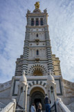 <center>Notre-Dame de la Garde</center>Entrée de la crypte. D'une hauteur de 41 mètres, le puissant clocher carré situé au-dessus du porche d'entrée comporte deux étages identiques formés de cinq arcatures, celle du milieu servant de fenêtre à un petit balcon. Cet ensemble est surmonté d'un beffroi dont chaque face est constituée de trois grandes baies aux colonnes de granit rouge derrière lesquelles sont placés les abat-sons.