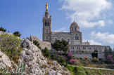 <center>Notre-Dame de la Garde</center>Vue du chemin du Bois sacré. En 1851, les Administrateurs de Notre-Dame de la Garde demandèrent au Ministre de la Guerre l’autorisation de démolir la petite chapelle et de la remplacer par un sanctuaire plus grand surmonté d’un haut clocher. Il donna son accord le 5 février 1852. Le sanctuaire actuel est l'oeuvre d'Henri Espérandieu,  de 1853 à 1874, en collaboration avec Henri Révoil pour le décor. La première pierre fut posée le 11 septembre 1853 par l’évêque de Marseille, Mgr Eugène de Mazenod. La basilique est de style romano-byzantin.