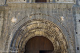 <center>Saint Guilhem le Désert. </center> Le porche comporte un portail en plein cintre qui présente trois voussures reposant sur des colonnes à chapiteaux décorés et qui creusent l'archivolte décorée d'une bande de dents d'engrenage. De part et d'autre, au-dessus du portail, se trouvent deux sculptures, une tête et un buste féminins, des remplois antiques.