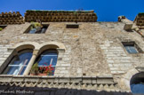 <center>Saint Guilhem le Désert. </center> A droite, un escalier conduit à l’étage mais, à l’origine, une porte permettait d’accéder au premier étage depuis la rue. Au-dessus de ces ouvertures court une frise de dents d’engrenage, surmontée par une imposte, l’ensemble permettant un jeu d’ombre et de lumière. Le premier étage voit le jour par trois fenêtres géminées. La maison, bâtie en pierre froide de petit appareil date certainement de la période de splendeur de l’abbaye et on peut supposer qu’elle appartenait à l’une des notabilités locales.