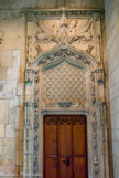 <center>Palais Jacques Coeur. </center> Le tympan fleurdelisé honore le roi Charles VII. Il est surmonté d'arcs en accolage prolongés d'un fleuron, bordés de choux frisés et encadrés de pinacles sur pilastres. La forme des arcs et les éléments de décoration qui l'entourent sont caractéristiques du style de la grand'maison : le gothique flamboyant.
Au-dessus des arcs, deux bas-reliefs nous montrent un cerf ailé, emblème de Charles VII, et une biche ailée, emblème de la reine Marie d'Anjou