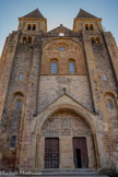 <center>L'église abbatiale Sainte-Foy</center>Le porche est encadré de deux tours aux contreforts puissants. Ces tours massives ont été surélevées et surmontées de pyramides de pierre en 1881. Elles ont deux ouvertures géminées dans leur partie supérieure que surmonte un toit quadrangulaire. Le portail occidental de l'abbatiale Sainte-Foy s'ouvre sur deux portes que sépare un large trumeau. Un vaste tympan en plein cintre les surmonte, abrité sous un fronton saillant. Plus haut, sous un arc de décharge en plein cintre, deux fenêtres de même forme sont surmontées d'un oculus. Six rosaces en marqueterie polychrome de pierre accostent ces fenêtres. La façade est couronnée par un pignon à rampants peu inclinés.