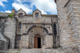 <center>Nasbinals. Église Sainte-Marie. </center>La façade méridionale qu'entourait, il y a une quarantaine d'années, le clos du cimetière s'ouvre sur la nef par un portail inscrit dans le massif d'un petit porche formé par une double voussure  en plein cintre supportée par quatre colonnettes à chapiteaux . Trois des chapiteaux sont sculptés de feuillage, le quatrième présente le combat d'un archer et d'un lancier