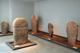 <center>Le musée Fenaille </center>Les statues-menhirs. Les hommes portent des armes et un baudrier en travers de la poitrine, maintenu à l’arrière par une bretelle qui rejoint la ceinture ; un accessoire de forme triangulaire et pourvu d’un anneau y est suspendu. Cet instrument étant difficilement identifiable, certains archéologues lui ont donné le nom d’objet
La datation des statues-menhirs rouergates est délicate, car toutes ont été retrouvées isolées en pleine nature. Toutefois, en comparant certains attributs figurés sur les statues avec des objets trouvés en fouille, on peut proposer avec vraisemblance la période comprise entre 3 300 et 2 200 av.J.C.