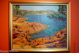 <center></center>Les roches rouges
Mauriac Eliot
(1862, Paris – 1945, Epinay-sous-Sénart)
1895, huile sur toile, 65 x 81 cm. Collection particulière.
Artiste polyvalent, Maurice Eliot consacre plusieurs huiles sur toile et un pastel au Saint-Pilon, au pic du Cap Roux et au Peysserin, observés depuis Camp Long. La quête d'éclat y est constante, quelle que soit la technique employée. L'artiste s'attache à capter les modulations dorées de la lumière sur le minéral et les Rocs, dan» une veine impressionniste, voire néo- impressionniste, en procédant par une succession de petites touches qui construisent les différents plans sur une hase chromatique initialement uniforme. Occupant une place prépondérante au premier plan, les rochers du littoral entrent subtilement en résonance avec les sommets crénelés qui se profilent au lointain.