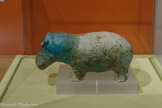 <center>Reflets du Nil</center>Statuette d’hippopotame.
Deuxième Période intermédiaire, 17e dynastie (1650-1550 av. notre ère) Faïence bleue, bleu-vert et noire GENÈVE, FONDATION GANDUR POUR L’ART.
<br> Herbivore d’ordinaire paisible, l’hippopotame charge avec fureur pour défendre son territoire et sa progéniture. Il est chassé dès le Prédynastique.
Incarnation redoutable de Seth, dieu de la violence et du chaos, il doit être massacré réellement et rituellement. La femelle gravide, divinisée en Thouéris, protège les femmes enceintes et promet une heureuse fécondité.
Sous forme de statuette funéraire, le cuir bleu couvert de fleurs évoquant l’eau et sa végétation, il symbolise la renaissance en plongeant puis surgissant du marais comme le dieu soleil hors du Noun. Les défunts s’approprient sa force combative maîtrisée comme puissance magique dans la Douat.