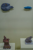 <center>Reflets du Nil</center>De haut en bas. De gauche à droite
Palette à fard stylisée en forme de tortue
Nagada I (3800-3500 av. notre ère)
Schiste
LYON, MUSÉE DES CONFLUENCES.
Durant les périodes prédynastiques, les tortues sont consommées puis deviennent taboues : elles sont associées aux forces du mal en raison de leur attrait pour l’obscurité. Cette espèce de tortue Trionyx triunguis, animal aquatique de grande taille, a un nez très reconnaissable en forme de trompe tubulaire. Elle est représentée dans l’Antiquité sur des palettes à fard rondes avec une petite tête ou sur des figurines.<br>
Figurine de poisson muge
Nouvel Empire, 18e-19e dynasties (1550-1186 av. notre ère) Faïence égyptienne bleue et noire LYON, MUSÉE DES BEAUX-ARTS.
Le poisson muge aussi appelé mugil cephalus est reconnaissable par ses écailles bleues grisâtres. Ici sous la forme d’une amulette, ce poisson pouvait atteindre 56 centimètres. Il était présent en mer Méditerranée mais remontait le long du fleuve pour vivre en eau douce. D’autres poissons, comme le barbeau, le tilapia ou la perche étaient communément consommés.<br>
Figurine d’Harpocrate à l’oie
Époque romaine (30 av. notre ère - 395)
Terre cuite
PARIS, MUSÉE DU LOUVRE.
L'oie, représentée dans des scènes nilotiques à l'époque pharaonique, est, dans le monde grec, un symbole de vigilance, de fécondité et de protection domestique. À l'époque où l'Égypte est sous domination grecque, associée à Harpocrate, forme hellénisée de Hor-pa-khered., « Horus l'enfant », fils d'Osiris et d'Isis, elle renforce l'idée de soin porté aux enfants. Ce dieu est représenté nu, avec la mèche de l’enfance et le doigt porté à la bouche. L'ensemble de la composition exprime ainsi le souhait d’une croissance heureuse, ainsi que la fécondité et la prospérité du foyer. <br>
Statuette de batracien, crapaud ou grenouille Époque romaine (30 av. notre ère - 395)
Serpentinite
GENÈVE, FONDATION GANDUR POUR L’ART.
Les grenouilles sortent en grand nombre de l’eau lorsque le Nil est au plus bas. Leurs croassements semblent annoncer l’arrivée prochaine de la crue. Ils sont évoqués dans l’Hymne à Hâpy, destiné à. favoriser la crue. Le hiéroglyphe de la grenouille signifie « qui renouvelle la vie». Les bonds prodigieux des grenouilles expriment le dynamisme, dont celui de la création, et leur étonnant pullulement, son renouvellement. Ainsi la nouvelle crue doit être puissante et dynamique mais non dévastatrice.