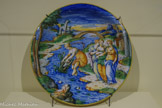 <center>Reflets du Nil</center>Moïse sauvé des eaux
Lyon ou Nevers 1535
Majolique, glaçure à l’étain ÉCOUEN, MUSÉE NATIONAL DE LA RENAISSANCE - CHÂTEAU D’ÉCOUEN.<br>
L’épisode religieux de Moïse sauvé des eaux est souvent représenté entre le 16e et le 18e siècle, sur des supports variés. Les conditions narratives offrent aux artistes la possibilité d’exploiter leur maîtrise du paysage et leur connaissance de l’Antiquité. Sur ce plat décoratif, l’artiste représente une vision idéalisée plus inspirée du monde gréco-romain.
