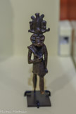 <center>Reflets du Nil</center>Figurine de Khnoum Basse Époque (664-332 av. notre ère) Alliage cuivreux
PARIS, MUSÉE DU LOUVRE. <br>
« Khnoum, seigneur d’Éléphantine » est le maître des eaux fraîches Qebehou qui entourent cette île, et de celles de la première cataracte, au sud de l'Égypte. Le lieu de séjour de Hâpy y est un double gouffre, kererty, sous son contrôle car « il fait venir la crue en son temps, ni trop grande ni trop faible » après en avoir retenu les eaux. Une stèle de Sehel, île voisine, le décrit les pieds sur le flot, tenant le verrou de la porte à deux battants qu'il va ouvrir pour le libérer en qualité de régulateur. Grâce à son intervention Hâpy s'épanche, la terre revit, les plantes croissent, promesse de nourriture. Dieu potier qui façonne les hommes sur son tour,  il « fait advenir tout ce qui existe » et entretient la vie.