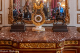 <center>Chambre sur cour.</center>Pendule Bourdier. 1775-1791. Pendule en forme de lyre en bronze ciselé et doré montée sur une base ovale en marbre blanc dont les quatre pieds aplatis reposent sur un socle en marbre. Cette base, bordée d'une double rangée de perles, entourée de chaînes à glands, est ornée sur sa face antérieure d'un motif de lauriers entrecroisés accompagnant un médaillon qui renferme deux cœurs enflammés. Les montants de la lyre, ornés de perles, s'enveloppent chacun à leur base d'une large feuille d'acanthe, rattachées l'une à l'autre à leur base par un ruban terminé par trois glands. Chacun des montants se termine par une tête d'aigle qui tient dans son bec une guirlande retombant agrémentée de fleurs et de fruits. Sur la traverse qui relie ces montants se dressent trois fleurs du soleil. La lentille est remplacée par un cercle de grosses perles qui vient battre autour du mouvement, maintenu entre les bras de la lyre par une tige invisible fixée à la base. <br>Statuette : Centaure Furietti jeune. 1750-1799. Le centaure jeune est représenté l'air joyeux, levant la main droite, tenant de la gauche une massue et, sur son avant-bras, une peau de sanglier. Il porte en croupe un amour ailé levant son bras droit. Le centaure âgé effectue un mouvement de tête vers l'arrière, il a les mains liées derrière son dos. Il porte en croupe un amour ailé tentant, de sa main gauche, de lui attraper les cheveux.  Les centaures Furietti originaux portent le nom du cardinal qui, en 1736, les découvrit lors des fouilles de la villa d'Hadrien à Tivoli. Ils sont achetés par le pape Clément XIII en 1765 et rejoignent les collections des musées du Capitole. Ces bronzes monumentaux jouissent d'une grande notoriété au cours de la seconde moitié du XVIIIe siècle, et sont régulièrement copiés. En effet, ils répondaient au goût de l'époque pour les pendants. Ainsi, les deux centaures Furietti présentés dans l'Hôtel de la Marine sont des réductions XVIIIe des originaux romain..